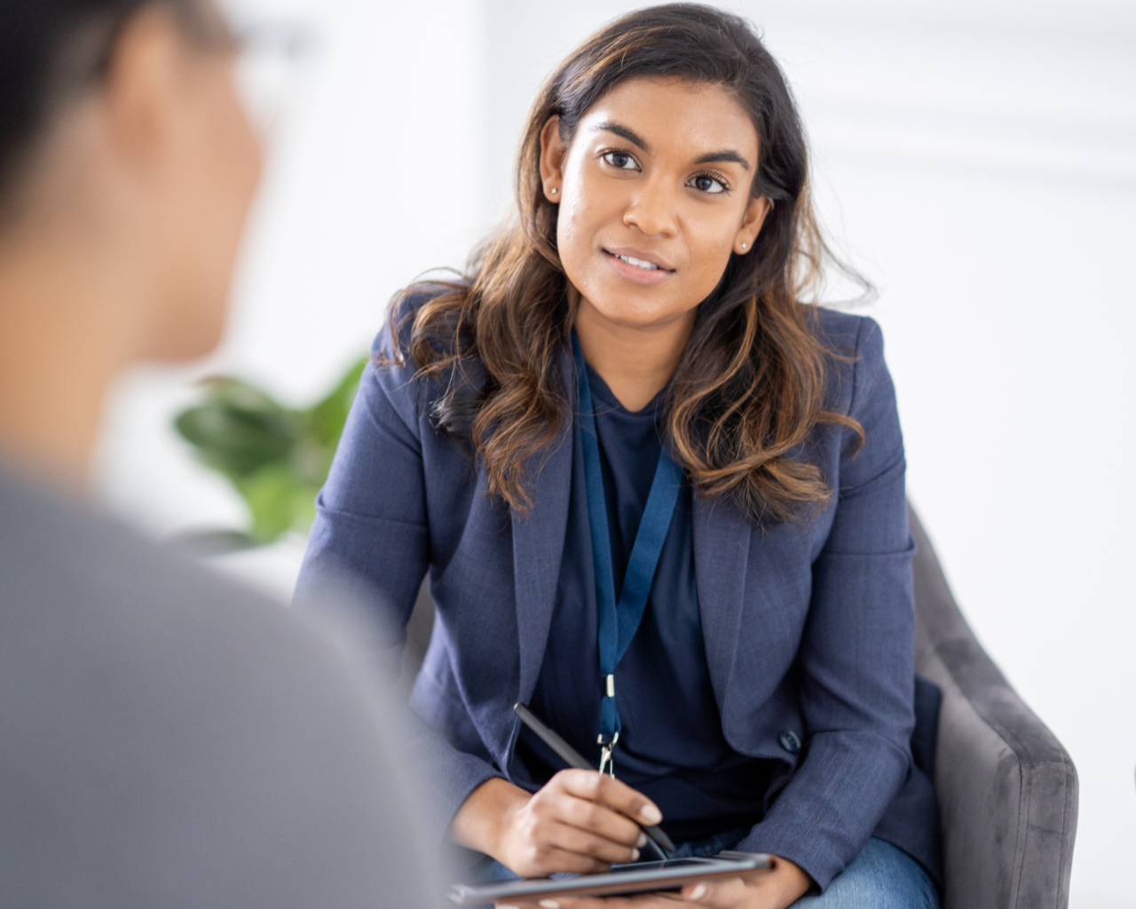 woman sitting with tablet and pen in her hands talking to another person